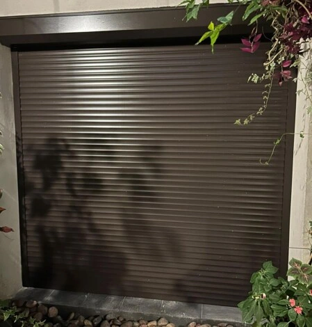 Cortina catalana de aluminio pintada símil madera instalada en fachada residencial, combinando diseño clásico, textura cálida y protección reforzada